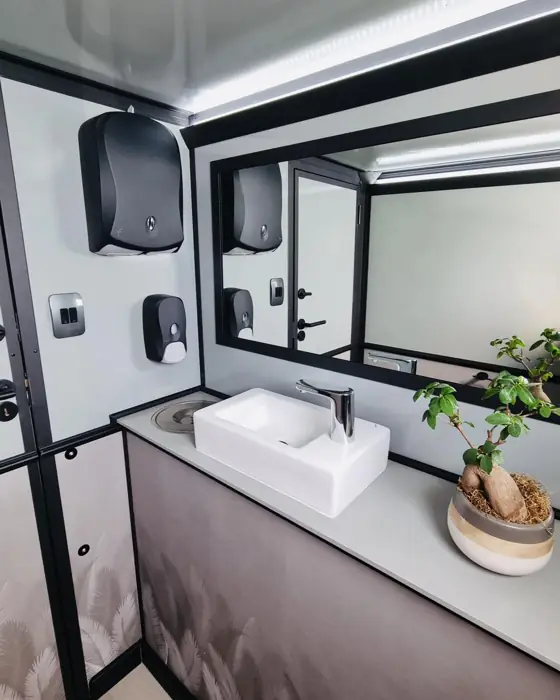 Restroom trailer stall with large mirror, sink and paper towel dispenser