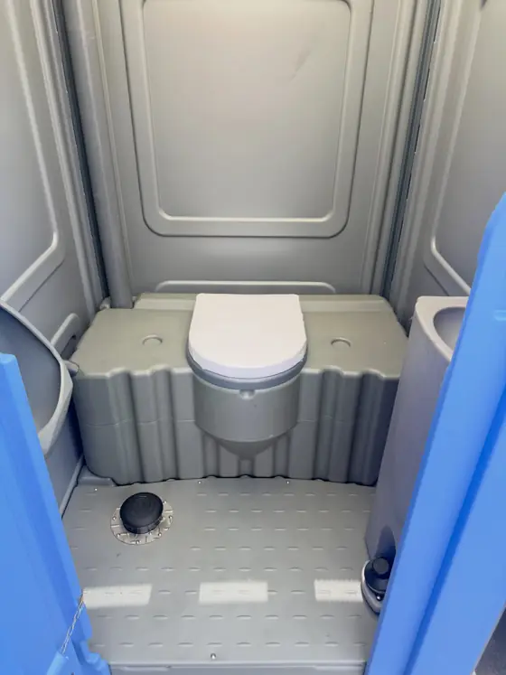Inside a standard porta potty: gray seat with lid and white tank liner