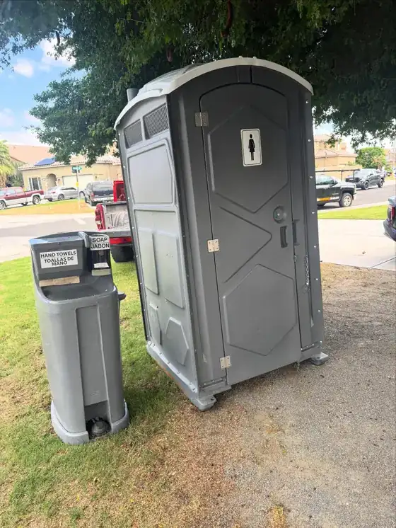 Gray porta potty with a hand wash station on a lawn